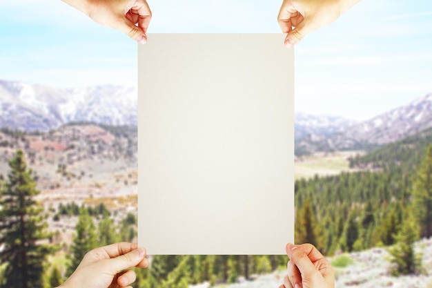 Four hands holding blank poster on landscape background Mock up