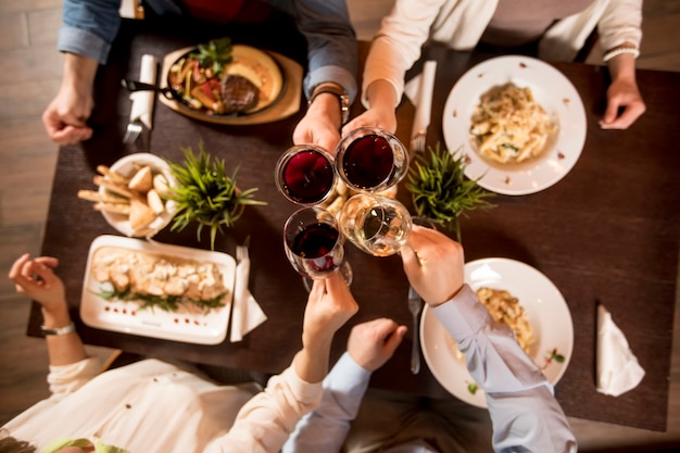 Photo four hands with red wine toasting over served table with food