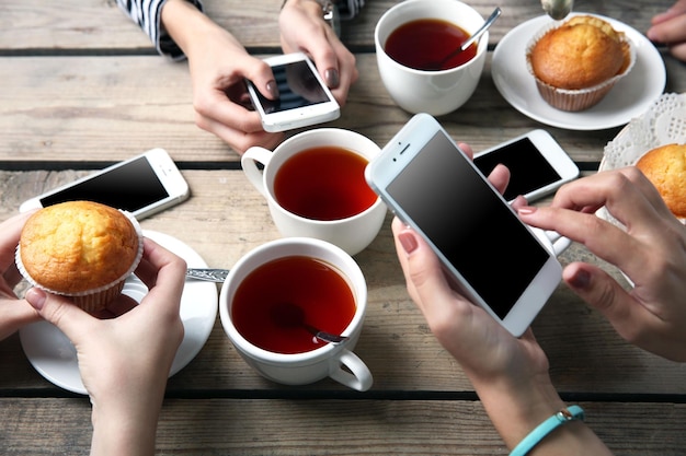 Photo four hands with smart phones holding cups with tea on wooden table background