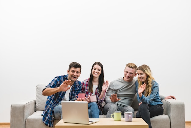 The four happy people gesture near laptop on the white wall background