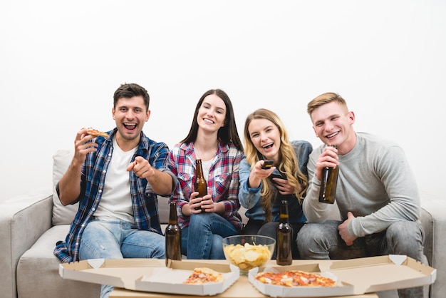 4人の幸せな人々は白い背景にピザとビールでテレビを見ます