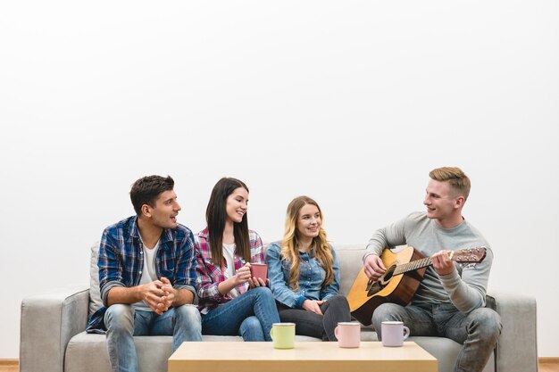 The four happy people with a guitar sit on the sofa on the white wall background