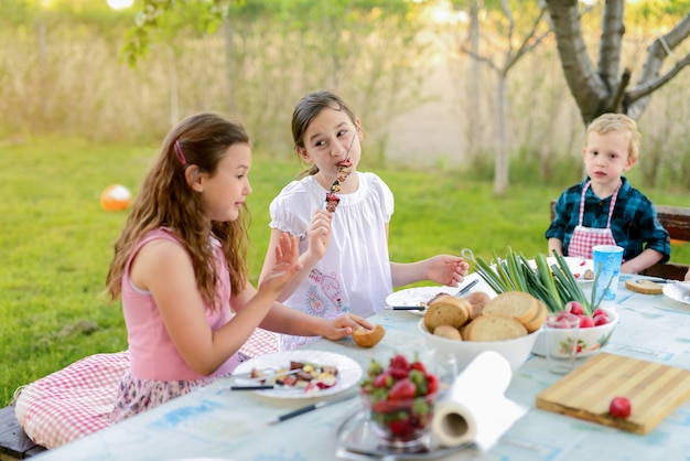 自然の中でテーブルのそばに座って食べている4人の子供