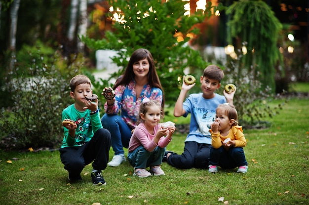 母親と一緒の4人の子供が夜の庭でドーナツを食べます。おいしいおいしいドーナツ料理。