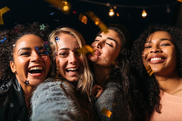 Photo four laughing girls taking selfie under confetti at night