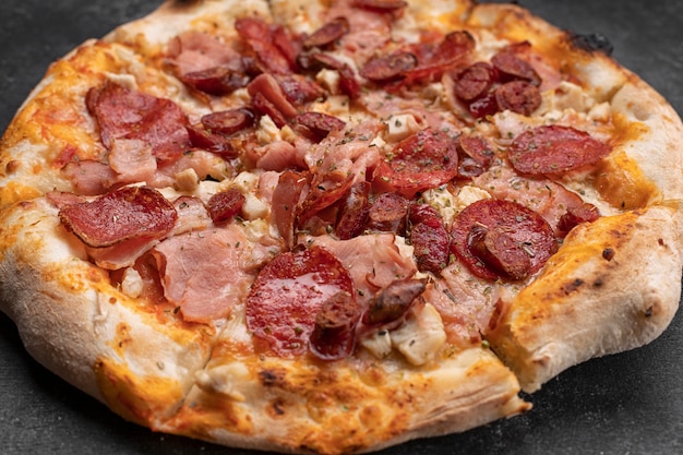 Four meat pizza with meat sausage ham and chicken on dark concrete