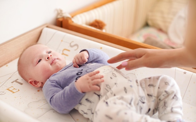 Four months old baby boy laying in bed ready for changing\
clothes, mother hands over him