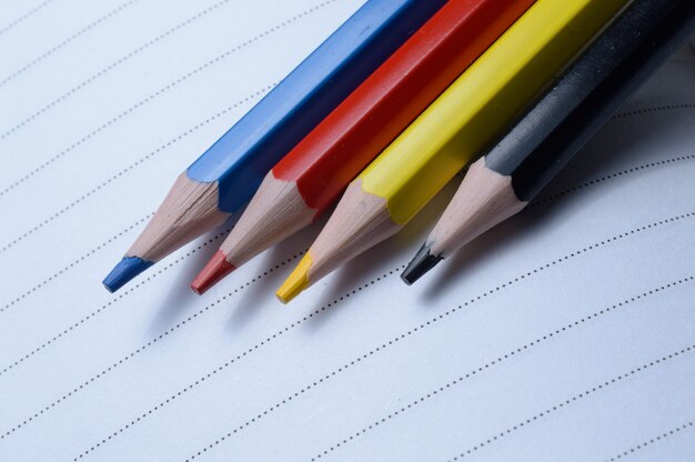 Four multi-colored pencils - blue, red, yellow, black. lie on an open notebook.