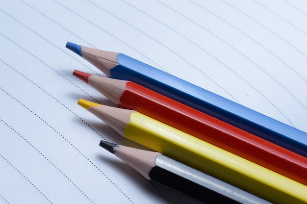 Four multi-colored pencils - blue, red, yellow, black. lie on an open notebook.