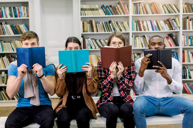 Photo four multiethnical friends students, two boys and two girls in casual wear, hiding faces behind open books