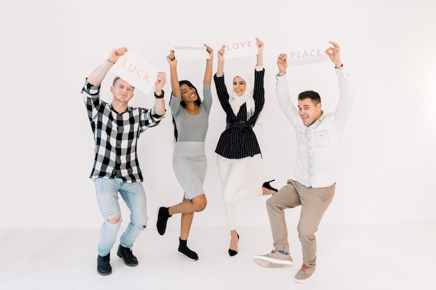 Four multiethnical young smiling people with placards and posters about love, peace and happiness, posing on white background