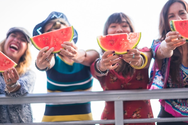 четыре милые счастливые молодые кавказские девушки едят арбуз, чтобы отпраздновать летний и теплый день с солнцем у океана