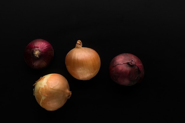 Four onions of red and gold colours on a black background top view