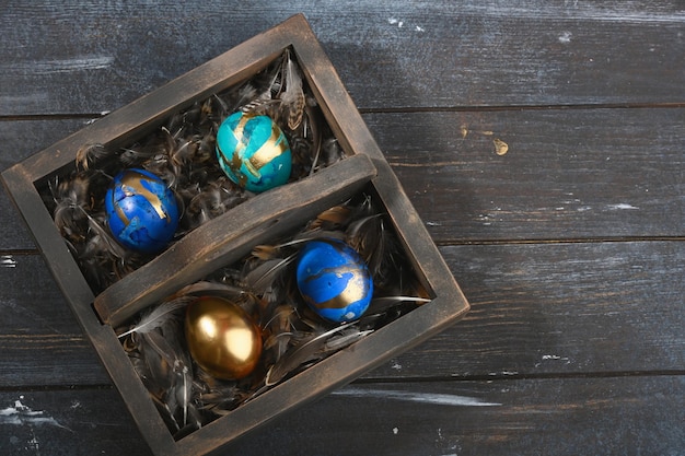 Четыре окрашенных цветных пасхальных яйца на шкуре животного в темной деревянной коробке на темном деревянном фоне в стиле Бохо