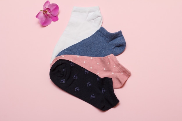 Four pairs of different women socks and orchid flower on a pink color background, Top view.