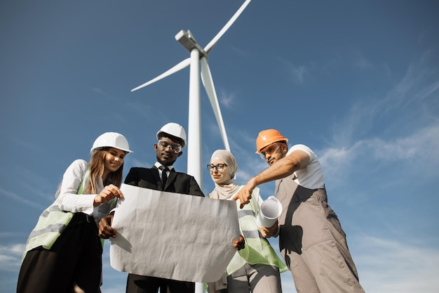 Four partners in helmets studying wind turbine blueprints