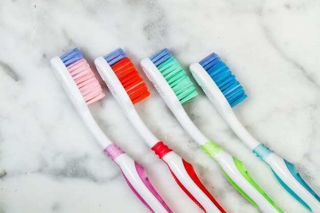 Four plastic colored toothbrushes on a marble table