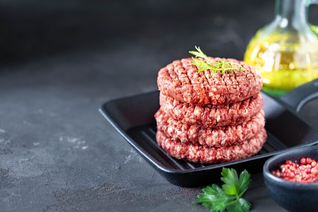 Photo four raw burger cutlets with chopped meat with salt, herbs and spices in a grill pan