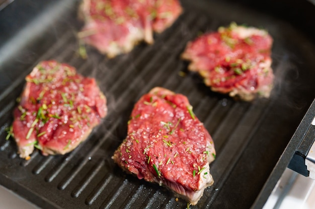 Four raw steaks are fried on a grilled pan