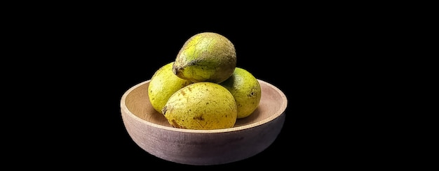 four ripe matoa fruit on a wooden bowl on a black background