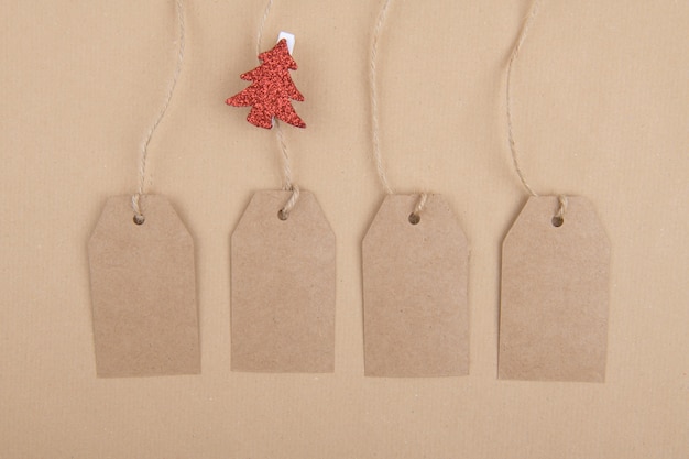 Foto quattro etichette di carta kraft riciclata appese a una corda con una molletta da bucato con un albero di natale rosso su carta kraft. lay piatto