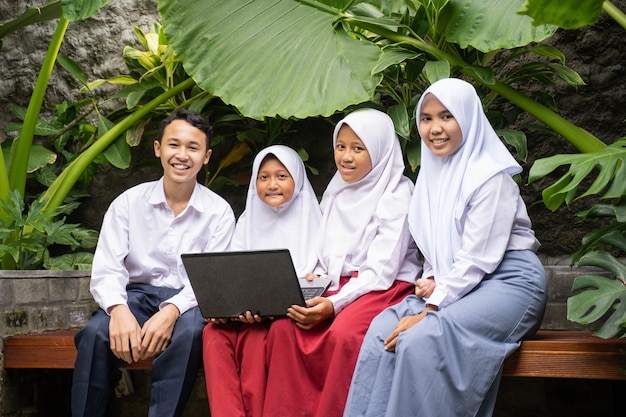 노트북을 사용하여 앉아있는 동안 교복을 입은 4 명의 청소년이 미소 짓습니다.
