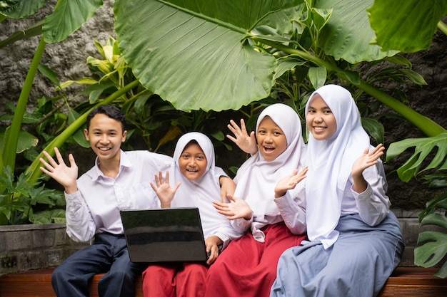 Four teenagers in school uniforms smiled at the camera with hand gestures while using a laptop