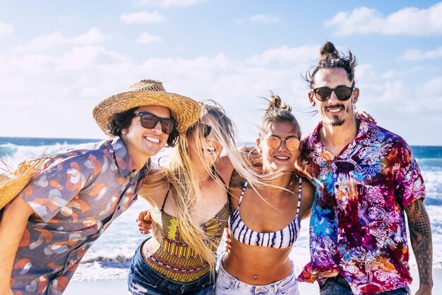 4 명의 관광 젊은이 백인 소년과 소녀의 유행 모양과 화려한 라이프 스타일 미소와 푸른 하늘과 바다가있는 해변에서 여름 휴가 휴가와 자유를 즐기십시오.