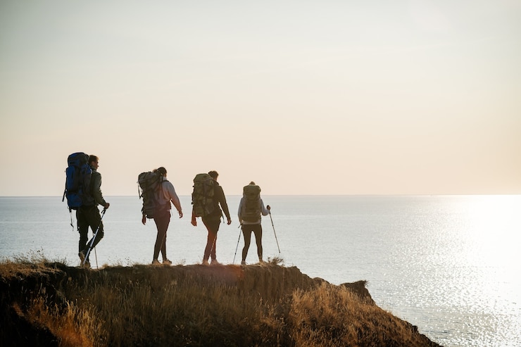 Photo the four travelers with backpacks walking on the mountain top near the sea