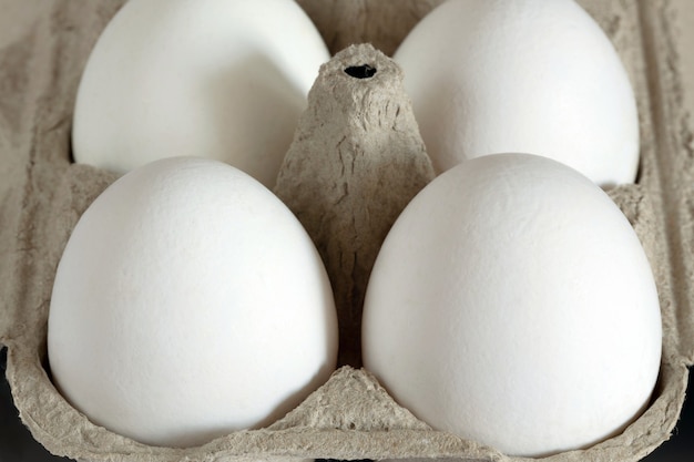 Четыре белых яйца помещены в светло-коричневую картонную коробку. Крупный план.