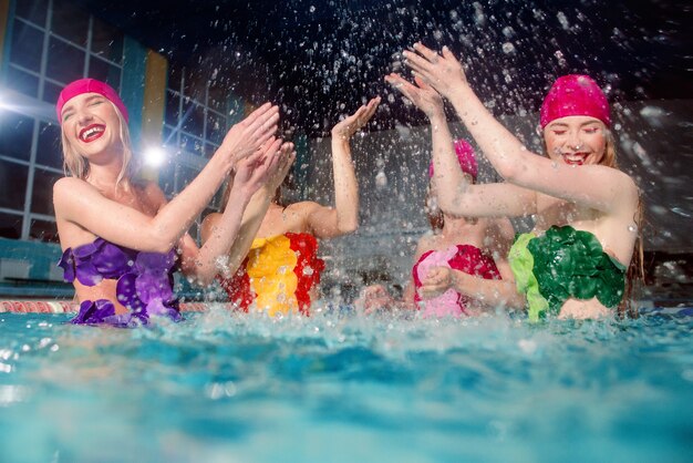 four women in colorful swimming suits and pink swimming hats in swimming pool