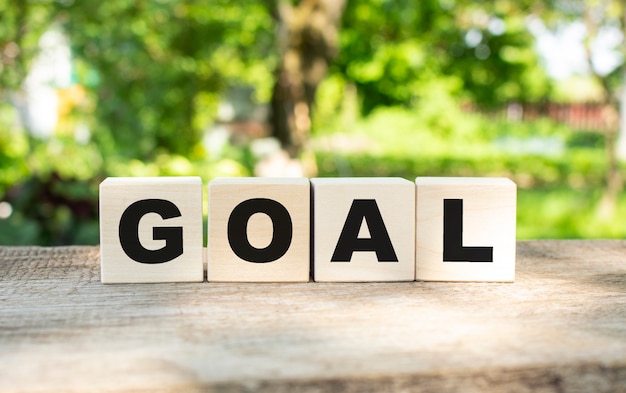 Four wooden blocks lie on a wooden table against the backdrop of a summer garden and create the word GOAL.