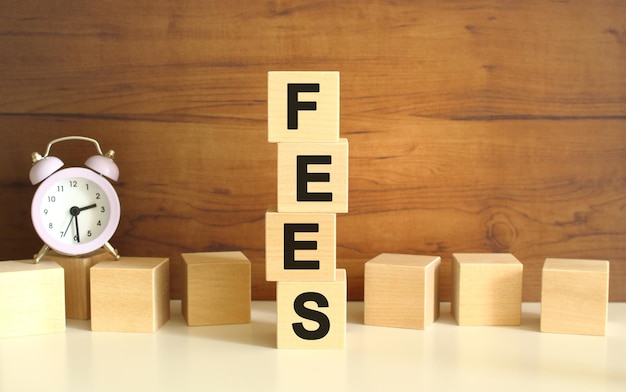 Four wooden cubes stacked vertically on a brown background form the word FEES