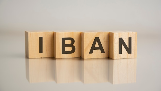 Four wooden cubes with letters IBAN. Business marketing concept. Reflection of the caption on the mirrored gray surface of the table. IBAN short for International Bank Account Number