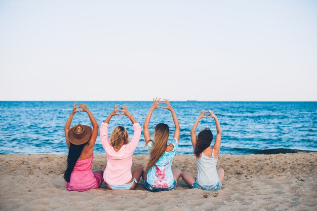Четыре молодые красивые шляпы девушки сидят на пляже