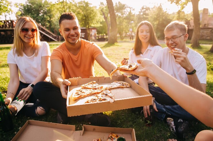 ピザを食べて、屋外でビールを飲む4人の若い陽気な友人。