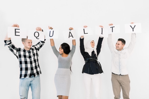 Photo four young diverse people of different races hold together paper posters with letters of the word equality, looking each other and smiling