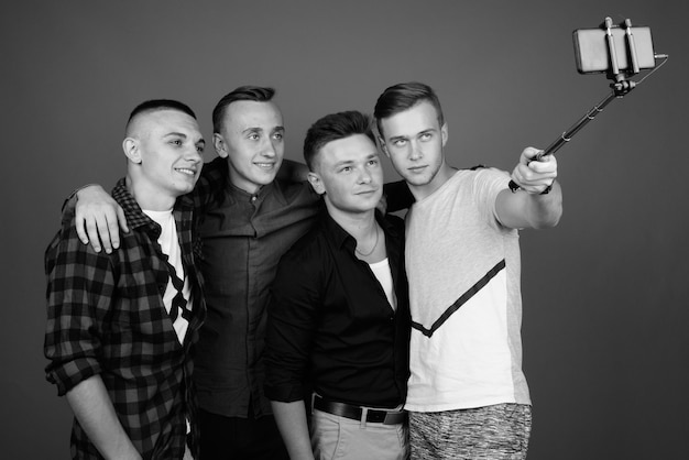 four young handsome men taking selfie together against gray wall. black and white