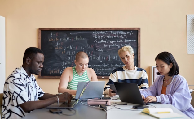 Photo four young intercultural coworkers in casualwear looking at screens of mobile gadgets while working individually over their new projects