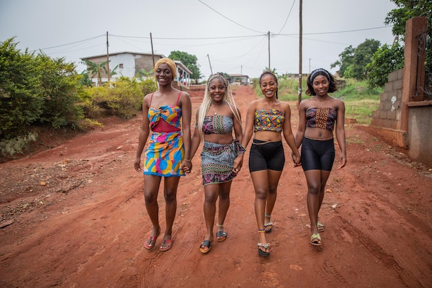 Four young smiling African women walk holding hands women dressed with traditional African clothes