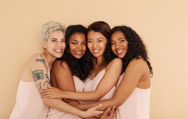 Four young smiling females embracing each other looking at camera in studio