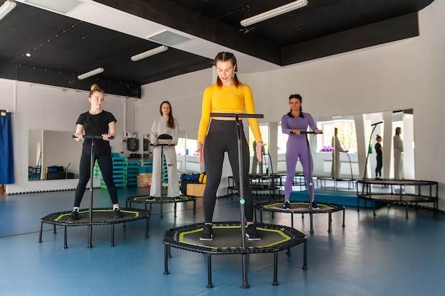 Four young women on trampoline young fitness girls trains on\
fitness studio