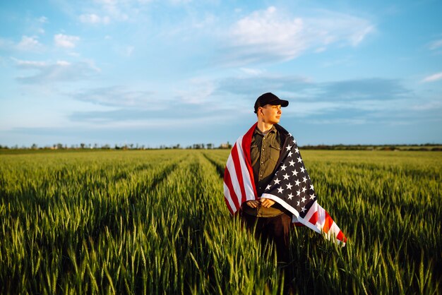 7月4日。フィールドにアメリカの国旗を持つ愛国心が強い男。若い男が誇らしげにアメリカの旗を振っています。独立記念日。