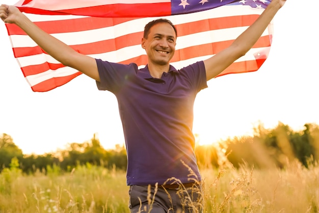 Четвертое июля. Патриотический человек с национальным американским флагом в поле. Молодой человек гордо машет американским флагом. День независимости.