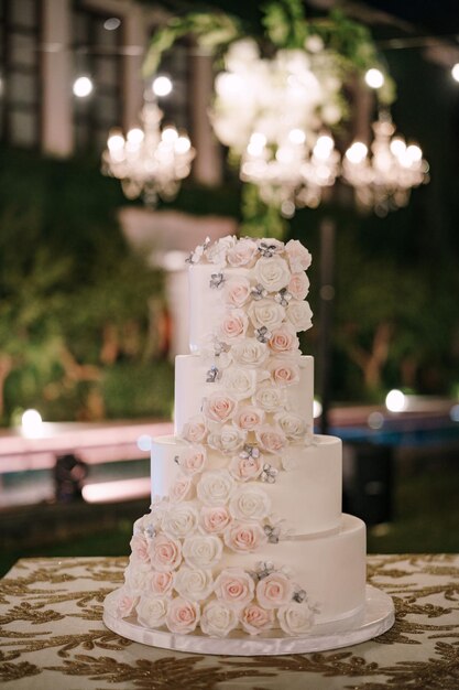 Fourtiered witte bruidstaart versierd met rozen staat op de tafel in de tuin