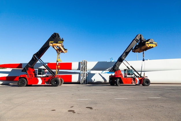 Fourwheeled mobile container loaders parked at seaport next to the storage blades for wind turbines