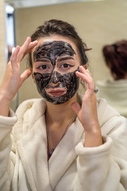 fragile lady puts a healing black mask on her face to improve her skin. The concept of improving the skin with a mask