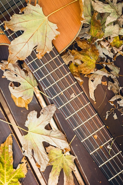 fragment of acoustic classical guitar with fall maple leaf on wooden background Autumn concert