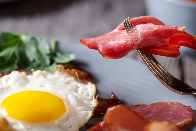Photo fragment of appetizing bacon on a fork and fried eggs