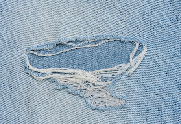 Frammento di tessuto jeans blu con un foro full frame da vicino